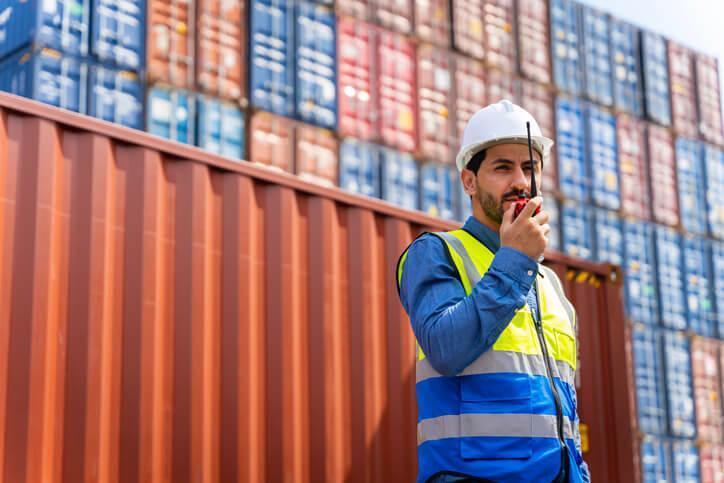 A male supply chain professional checking container orders at a shipyard after completing a logistics and supply chain diploma.