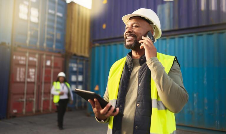 A smiling male supply chain and logistics professional at a shipyard after completing a logistics and supply chain diploma.