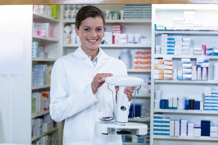 Cheerful female pharmacy assistant holding pharmaceutical balancing scales after completing her pharmacy assistant training