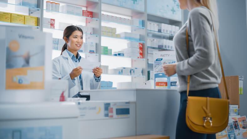 A pharmacy assistant training grad providing a prescription for a customer