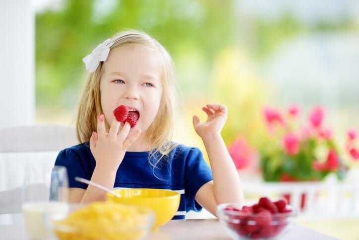 An early childcare assistant preparing snacks with a smiling female pupil