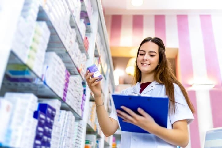 A pharmacy assistant organizing inventory behind the counter, showing one of the key responsibilities of a pharmacy assistant