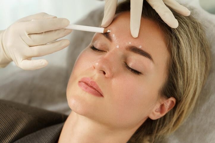 A female medical esthetician making marks on a client's face before filler injection after completing her medical esthetician training