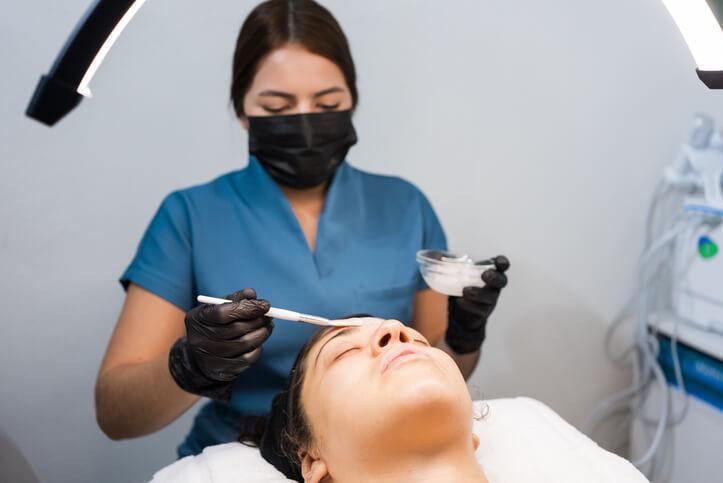 An esthetician wearing gloves and following hygiene procedures during a facial treatment An esthetician wearing gloves and following hygiene procedures during a facial treatment