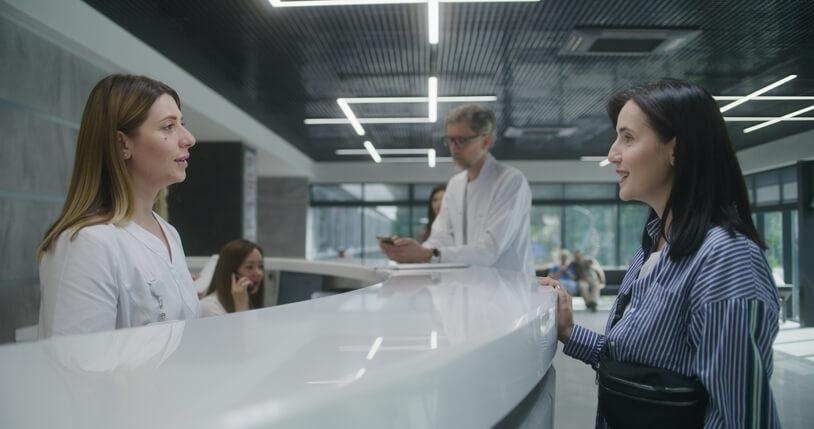 A medical office assistant training helping a patient at the front desk