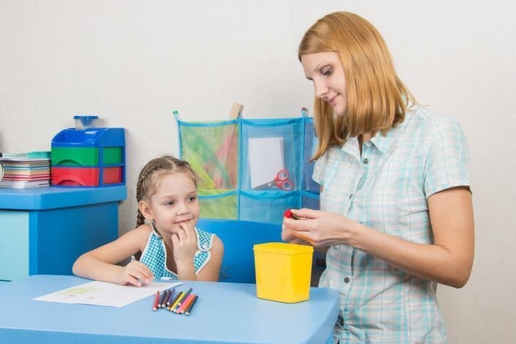 A female early childcare assistant sharpening a pencil for a female pupil