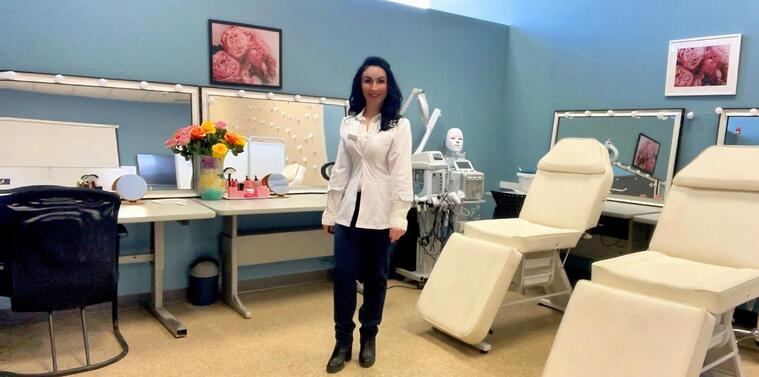 A medical esthetics training room with a smiling instructor, treatment chairs, and skincare equipment