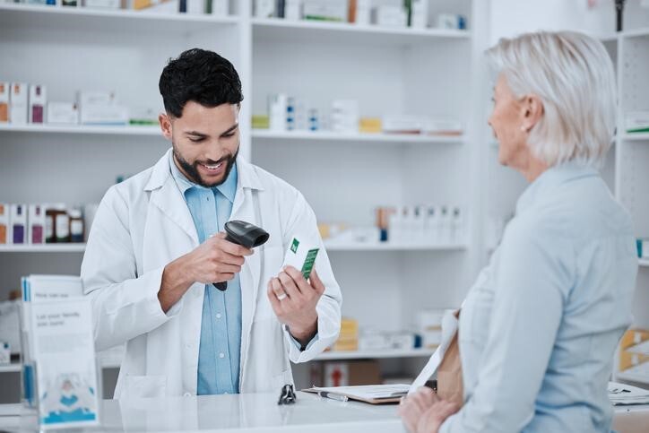 Cheerful male pharmacy assistant scanning the price of a customer’s prescription after completing his pharmacy assistant training