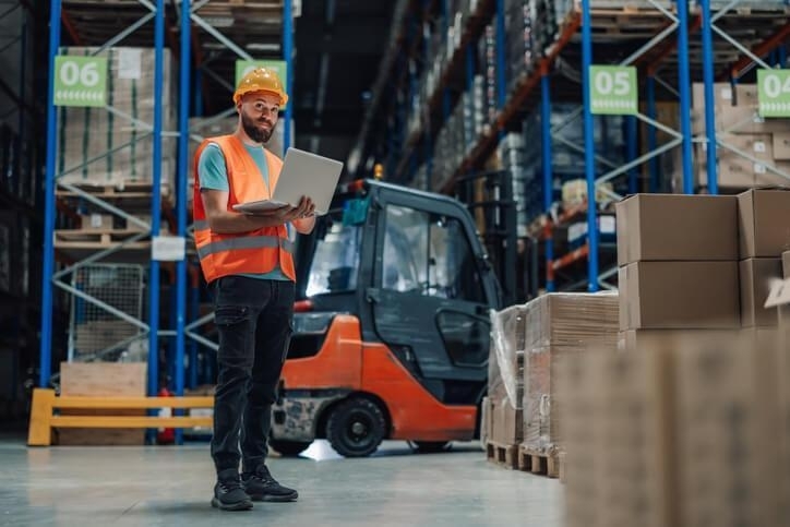 A supply chain and logistics grad completing inventory management on a laptop in the warehouse