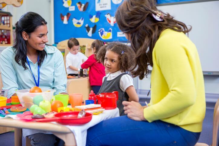 Two smiling early childcare assistants teaching a pupil about nutrition